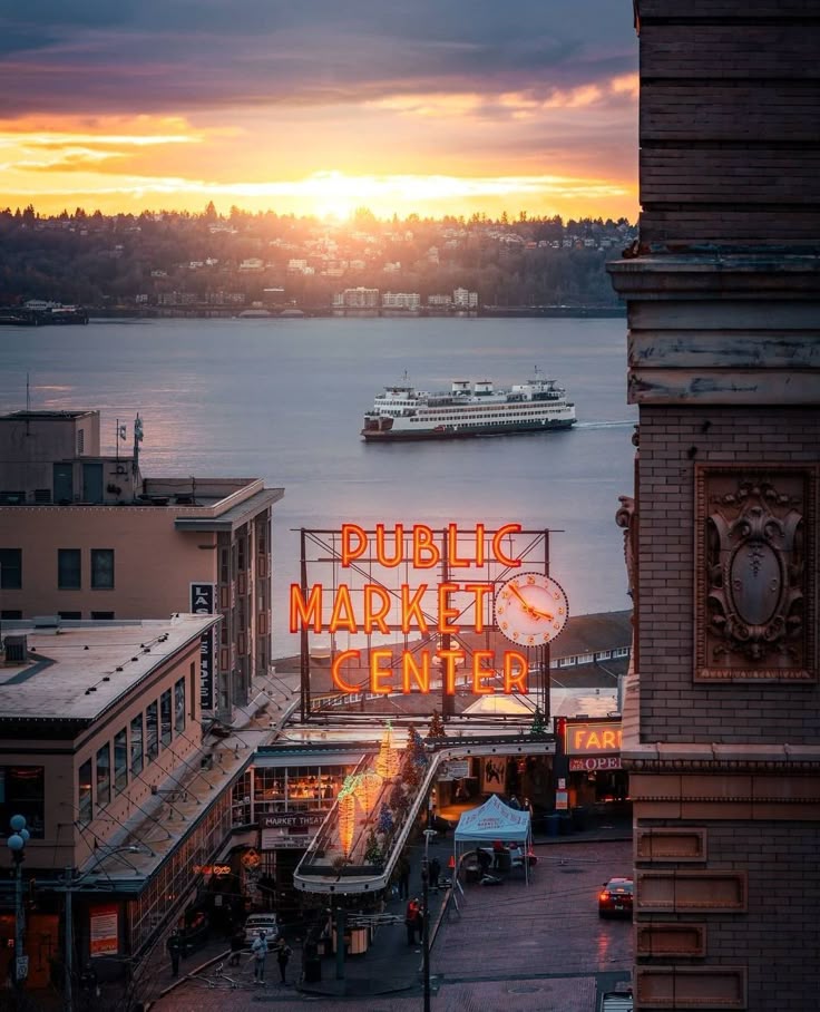 Seattle's Public Market Center sign, ferry on the water, and colorful sunset sky.