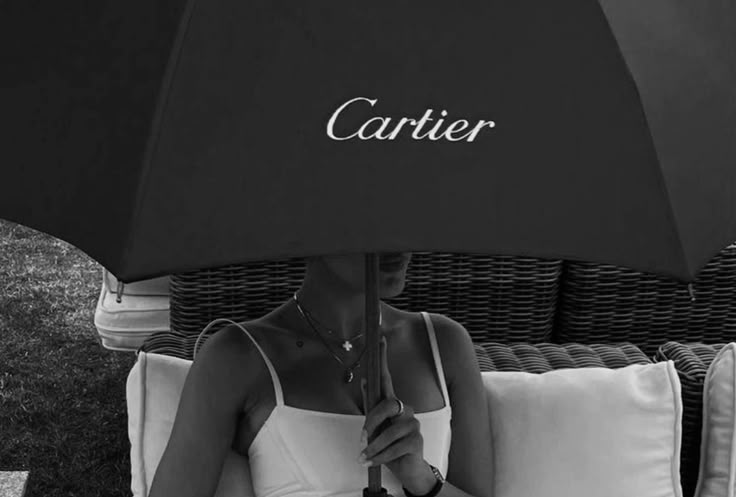 Person relaxing under a Cartier-branded umbrella, stylish and elegant outdoor scene.