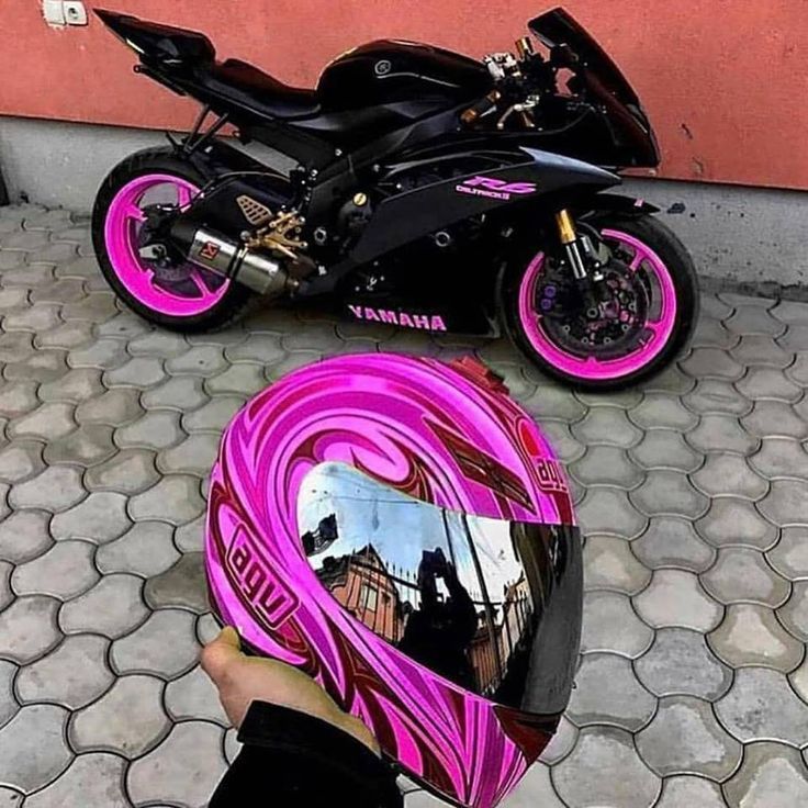 Black Yamaha motorcycle with pink accents and matching helmet on tiled pavement.