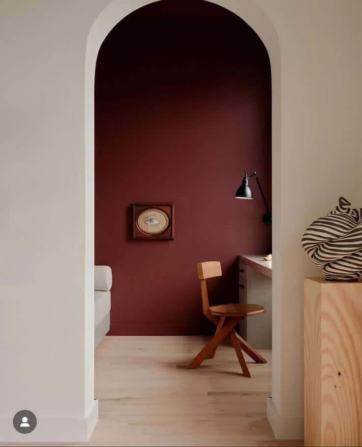 Minimalist study nook with wooden chair, desk lamp, and burgundy wall in archway design. Cozy and modern interior.