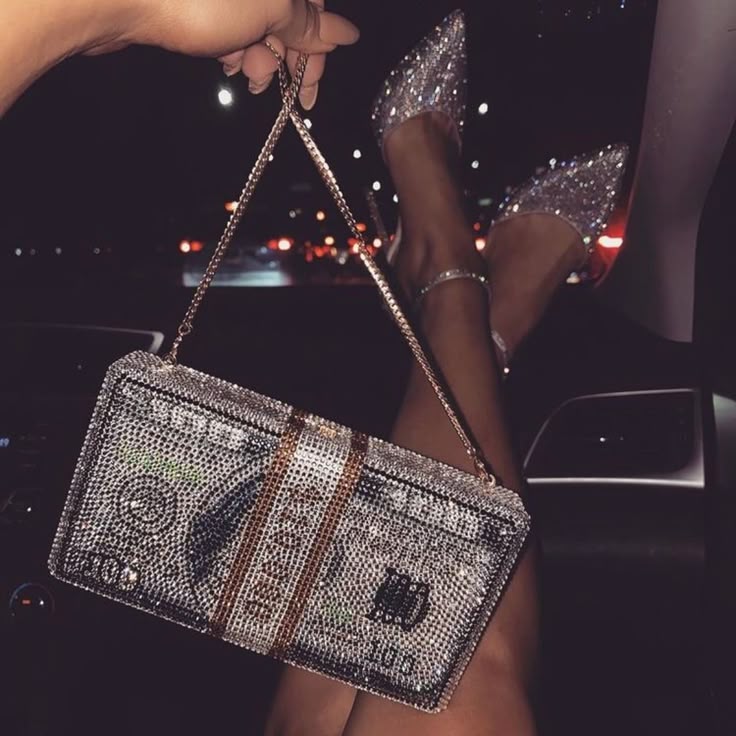 Glamorous rhinestone clutch shaped like a dollar bill, paired with sparkling heels and relaxed legs in a car.