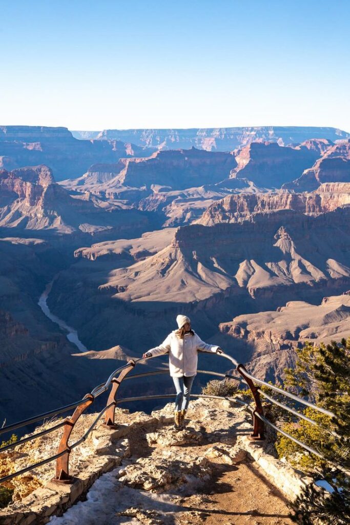 Person at the Grand Canyon viewpoint, enjoying breathtaking views and clear blue skies. Ideal travel adventure destination.