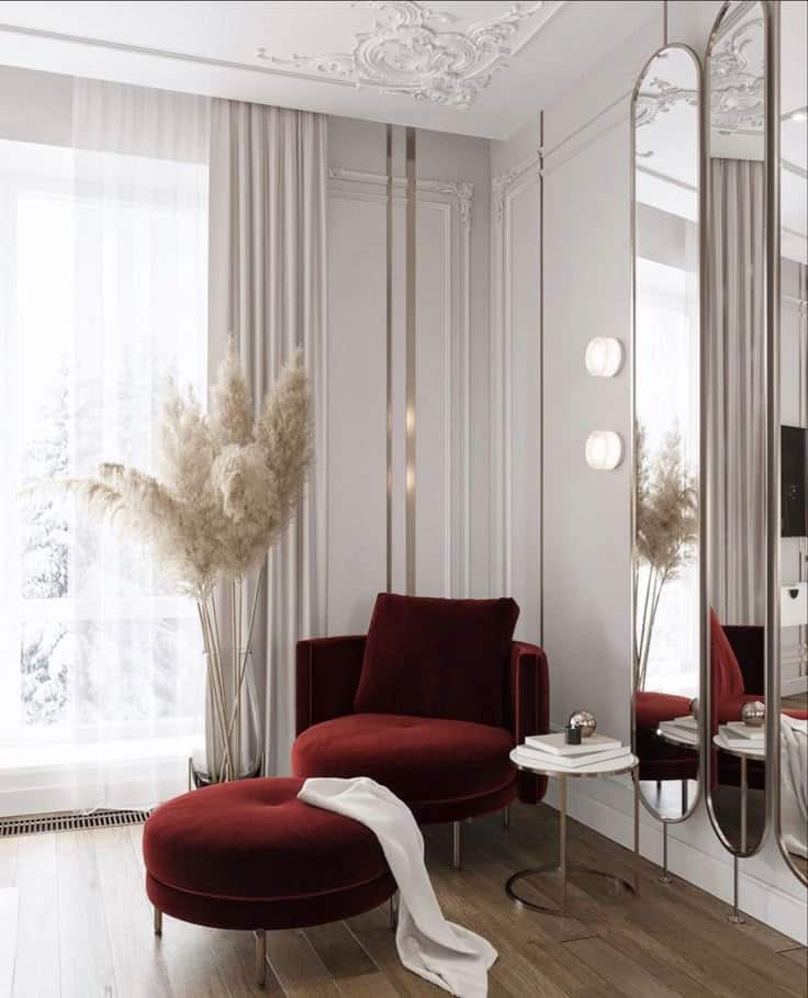 Elegant room with red velvet chair, matching ottoman, gold accents, and pampas grass by the window.