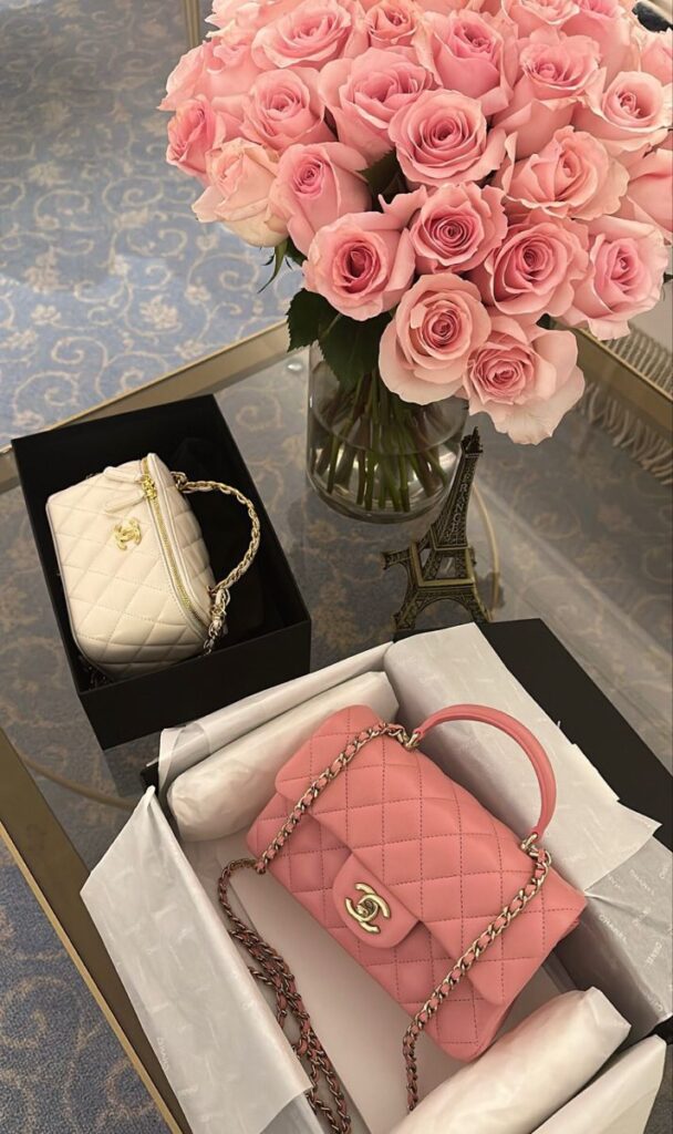 Pink and white luxury handbags with a bouquet of pink roses on a glass table.