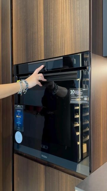 Person interacting with a modern black oven built into a wooden kitchen cabinet.