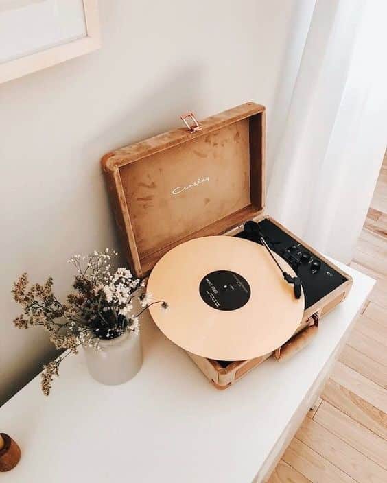 Vintage record player with beige vinyl spinning, next to a vase of dried flowers on a minimalist white table.