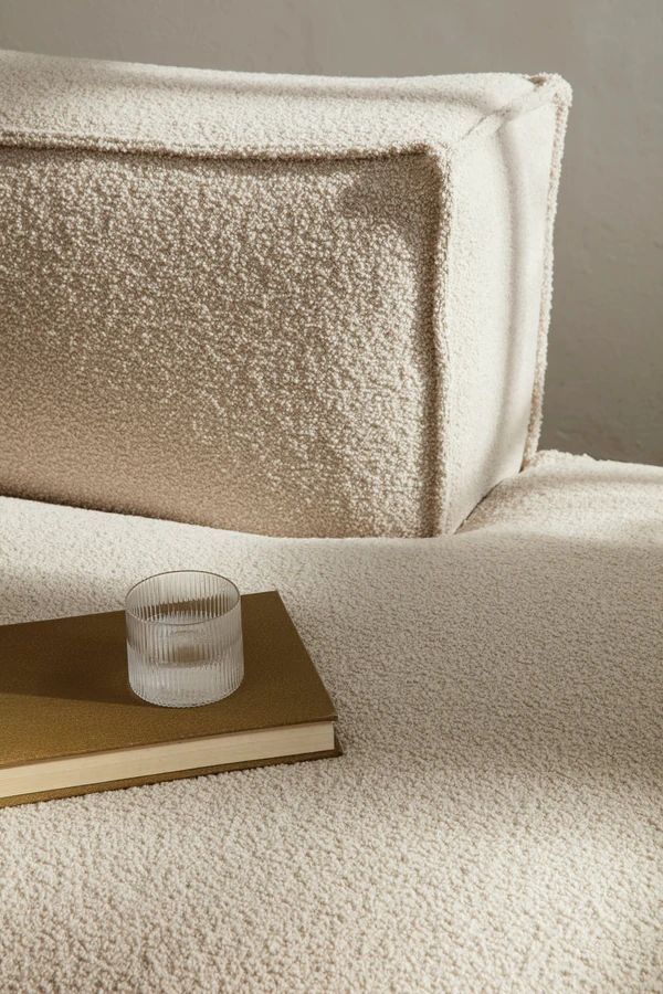 Beige textured sofa with a book and glass cup on the armrest. Cozy and minimalist home decor style.