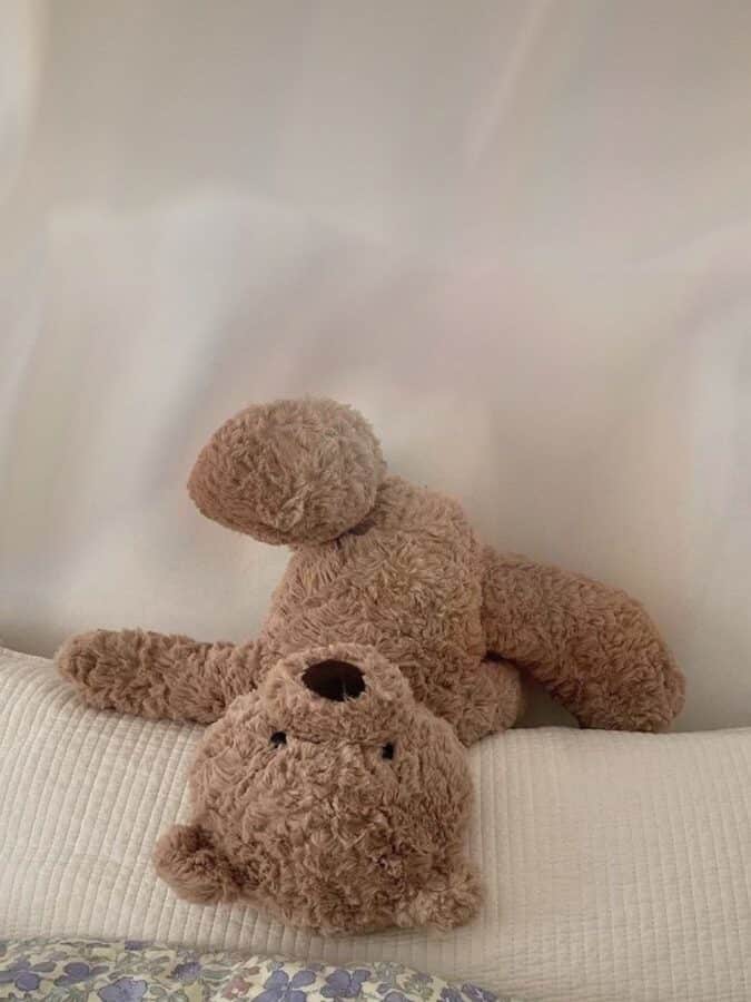 107d6e6d-7133-4947-abed-db332083a3bc Fluffy teddy bear lying upside down on a bed with a floral blanket, against a soft white background. | Sky Rye Design Fluffy teddy bear lying upside down on a bed with a floral blanket, against a soft white background.
