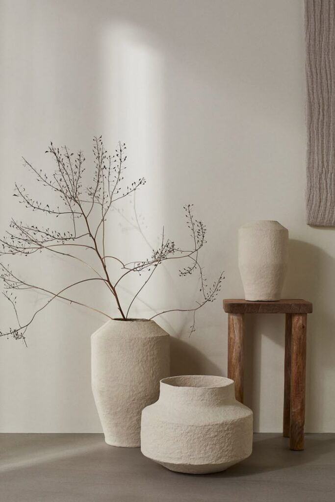Minimalist decor with textured vases and delicate branches on a wooden stool against a neutral wall.