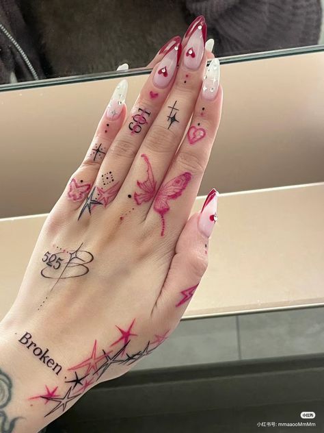 Intricate hand tattoos with butterfly, hearts, and Broken text, featuring detailed nail art.