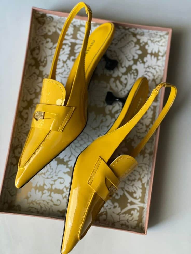Yellow pointed-toe slingback heels with shiny finish in an elegantly patterned shoe box.
