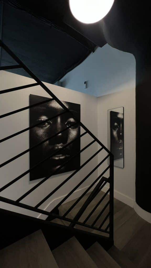 Abstract portraits displayed along a modern staircase, with black metal railing and unique interior lighting.