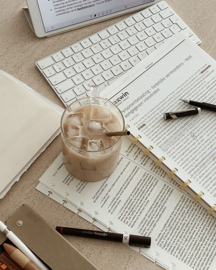 Iced coffee on a desk with keyboard, tablet, documents, and pens, creating a cozy workspace vibe.