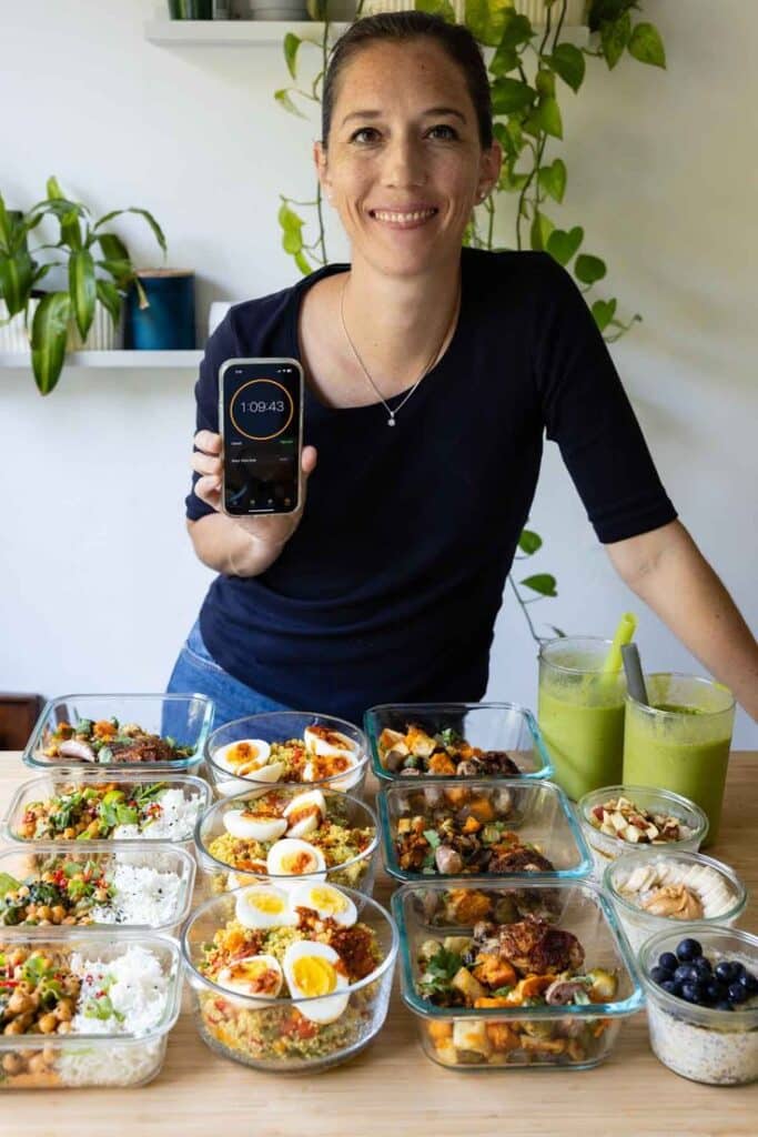 Person smiling with meal prep containers, holding stopwatch, showcasing healthy meal planning and organization.