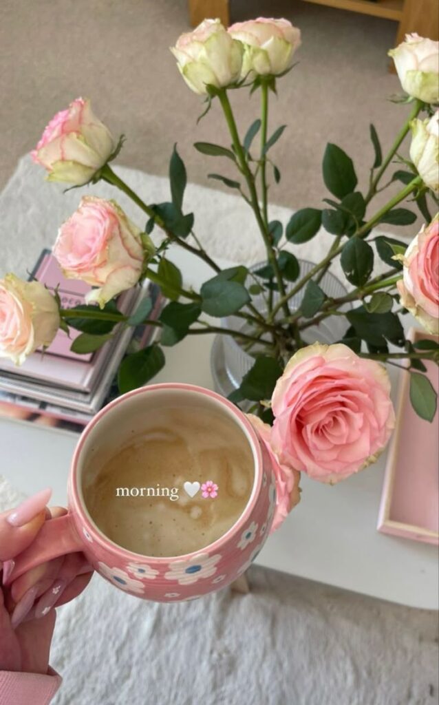 Pink rose bouquet beside a floral mug of coffee on a white table for a cozy morning atmosphere.