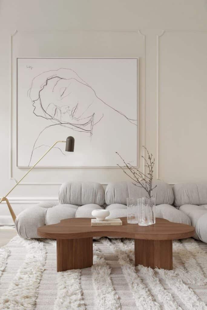 Minimalist living room with abstract line art, plush gray sofa, wooden coffee table, and textured rug.