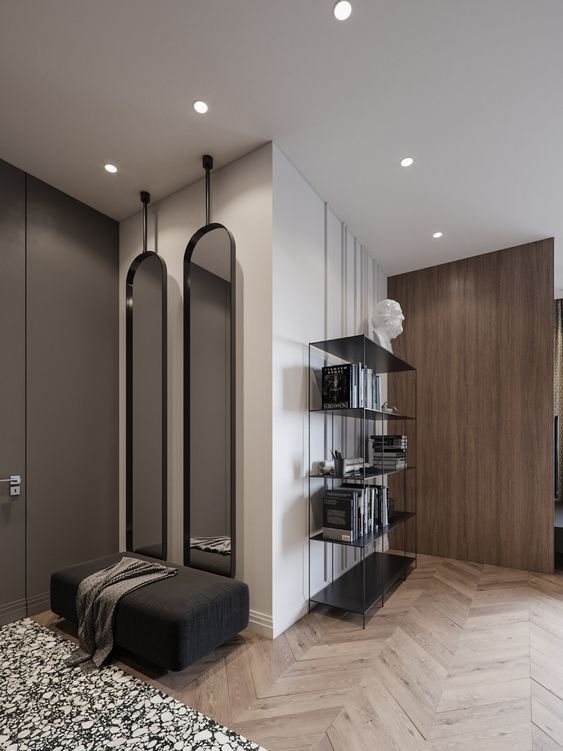 Modern minimalist bedroom with sleek mirrors, dark ottoman, wall shelves, and herringbone floor for stylish decor.