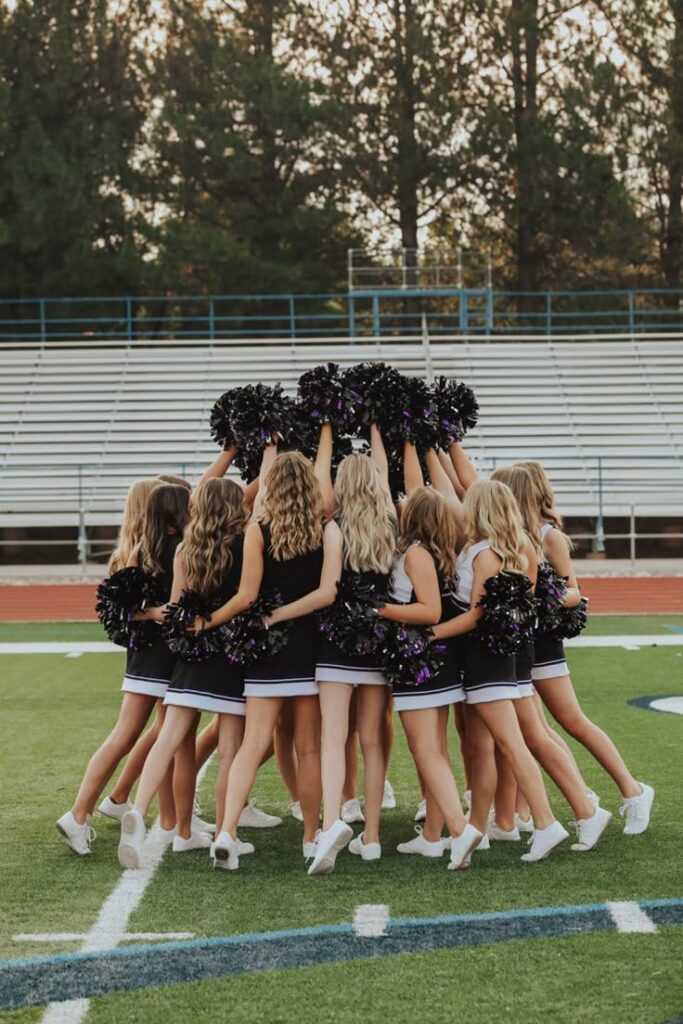 Cheerleading team huddles on a football field with pom-poms raised, showing team spirit and unity.