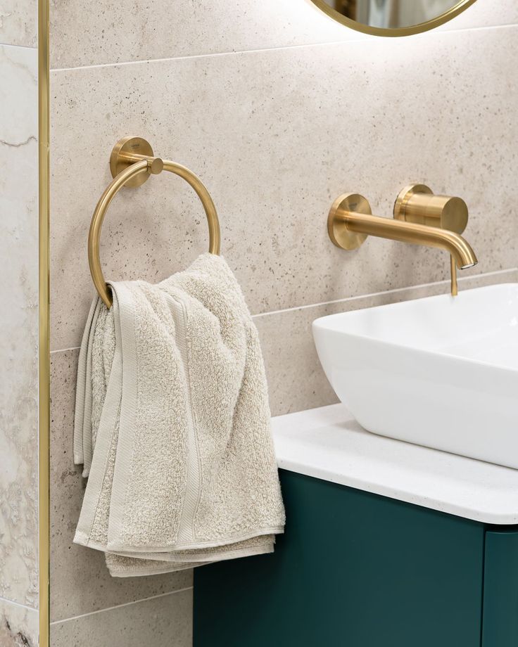 Luxurious bathroom with gold faucet, beige towel on a ring, and white countertop sink against cream tiled walls.