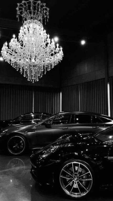 Luxury cars parked beneath an ornate chandelier in a dimly lit showroom.