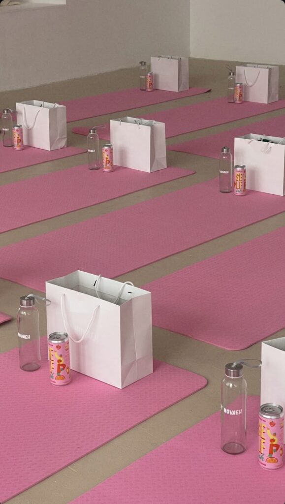Pink yoga mats with gift bags, water bottles, and cans arranged neatly in a studio setting.