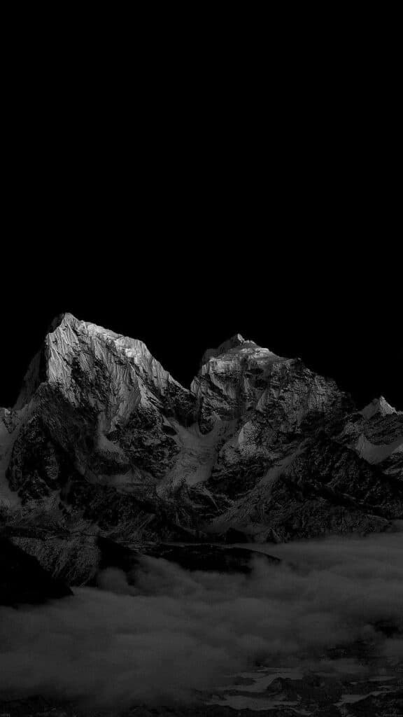 Dramatic black and white mountain peaks above misty clouds in a dark sky, highlighting nature's rugged beauty.