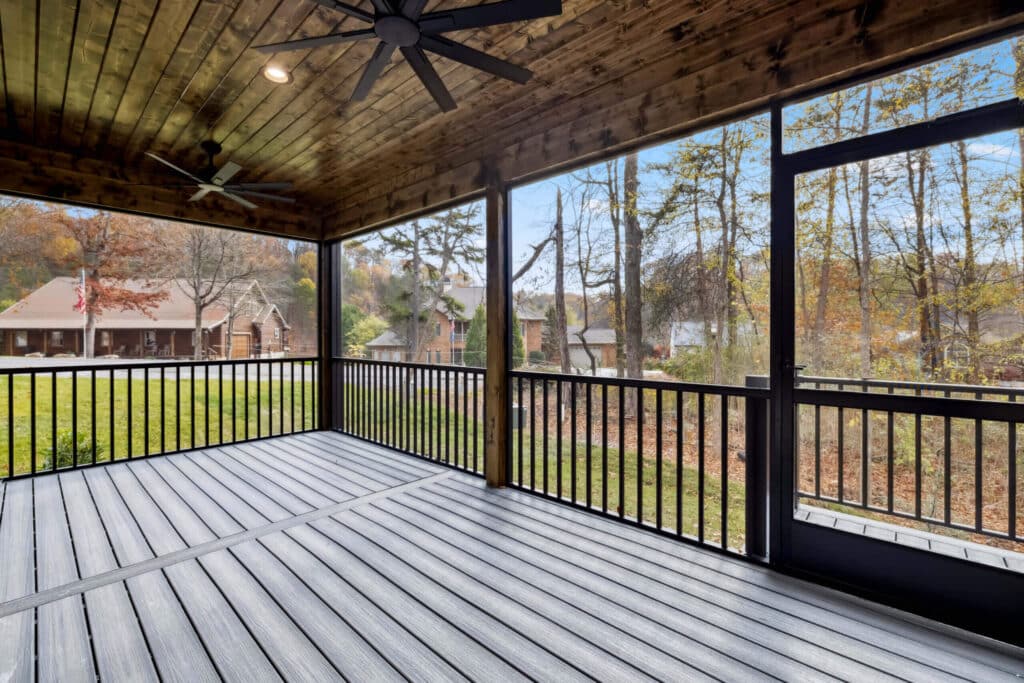Covered porch with ceiling fans and wooded view, featuring a wooden railing, ideal for outdoor relaxation.