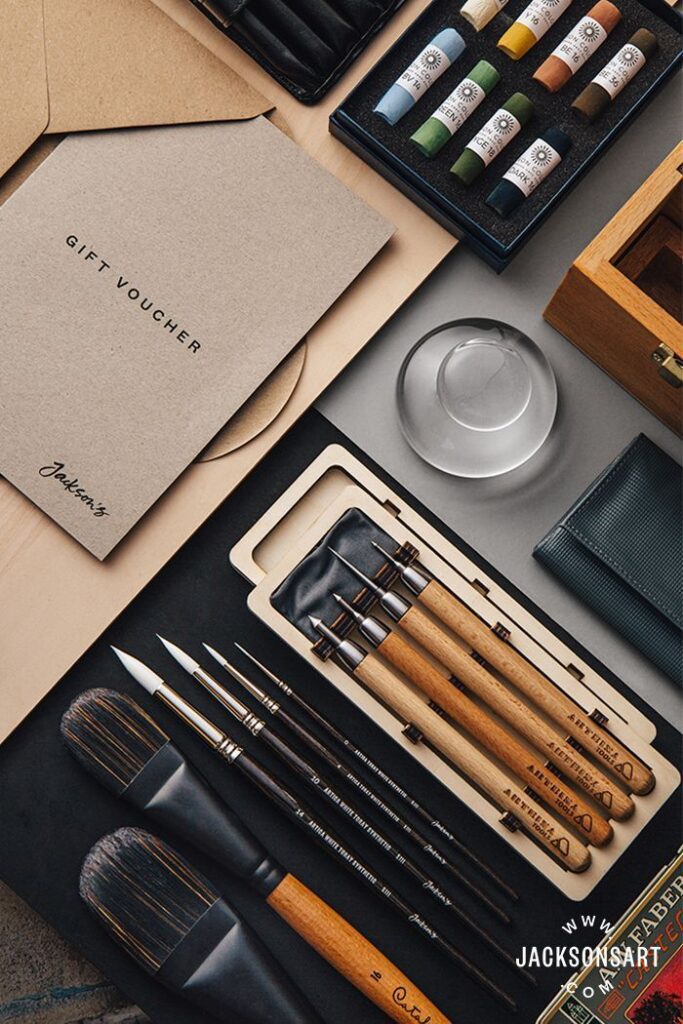 Art supplies including brushes and paints with a gift voucher from Jackson's Art, arranged artistically.