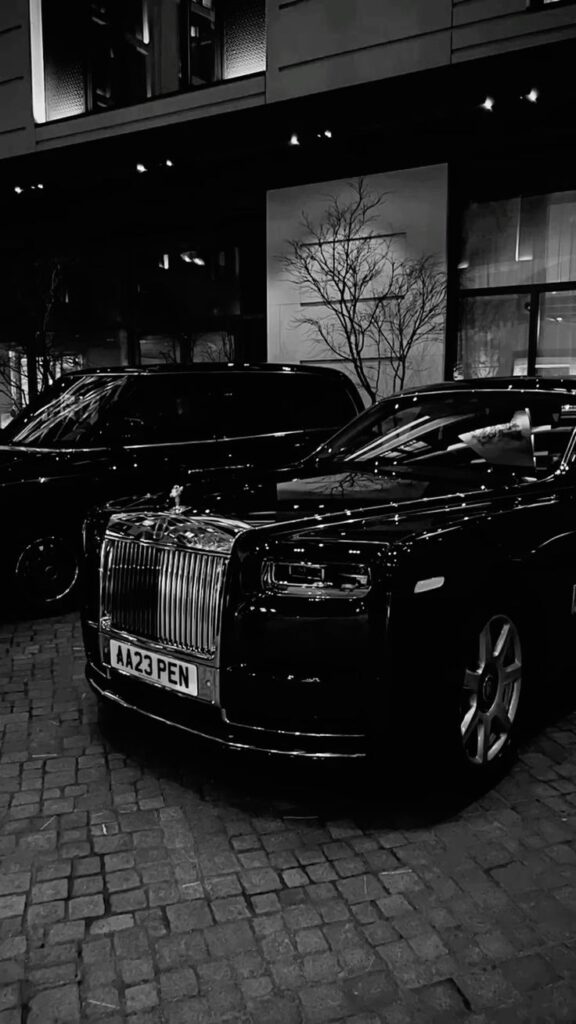 Black Rolls-Royce parked at night in a city setting with modern building backdrop.