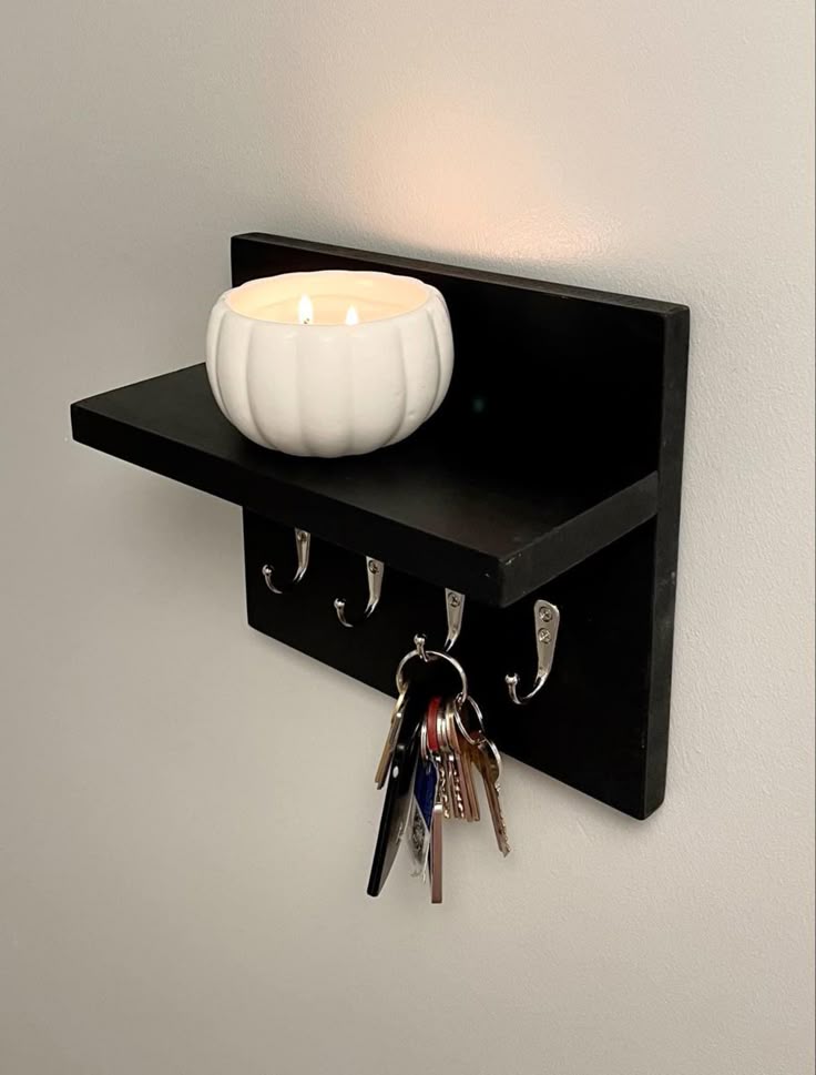 Wall-mounted shelf with hooks, holds a lit candle in a white holder and a keyring with keys for organized storage.
