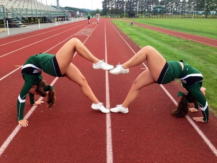 Two cheerleaders perform a bridge pose on a track, forming a heart shape with their bodies.