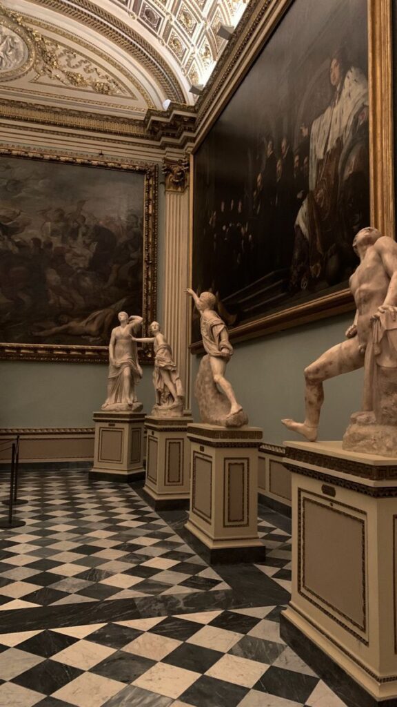 Elegant museum interior with classical sculptures and large paintings, showcasing intricate architectural details.