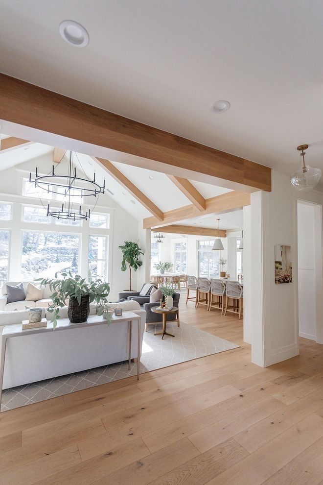 Spacious open-concept living room with wooden beams, modern decor, and large windows letting in natural light.