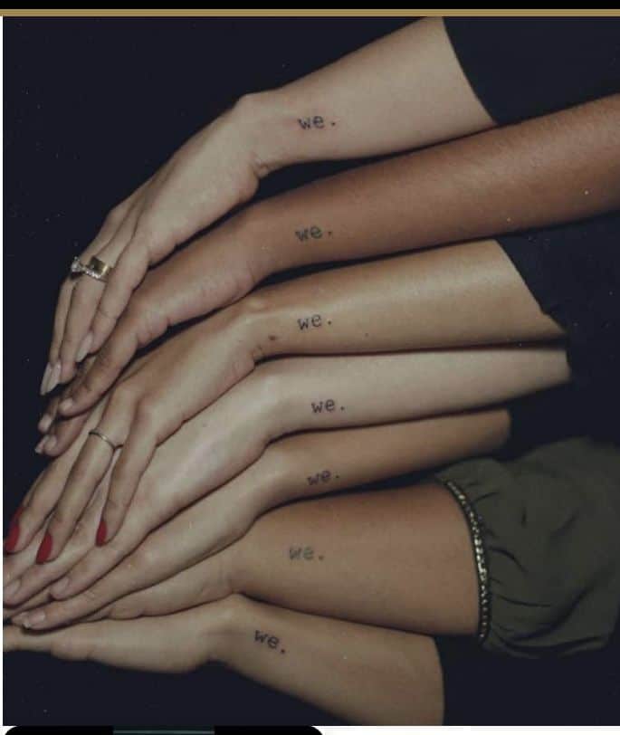 Five arms stacked, each with the minimalist tattoo we. symbolizing unity and connection across different people.