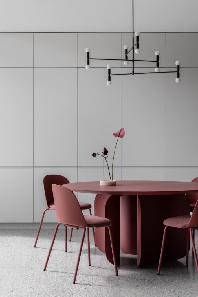 Minimalist dining area with round table, pink chairs, modern chandelier, and sleek gray cabinetry.