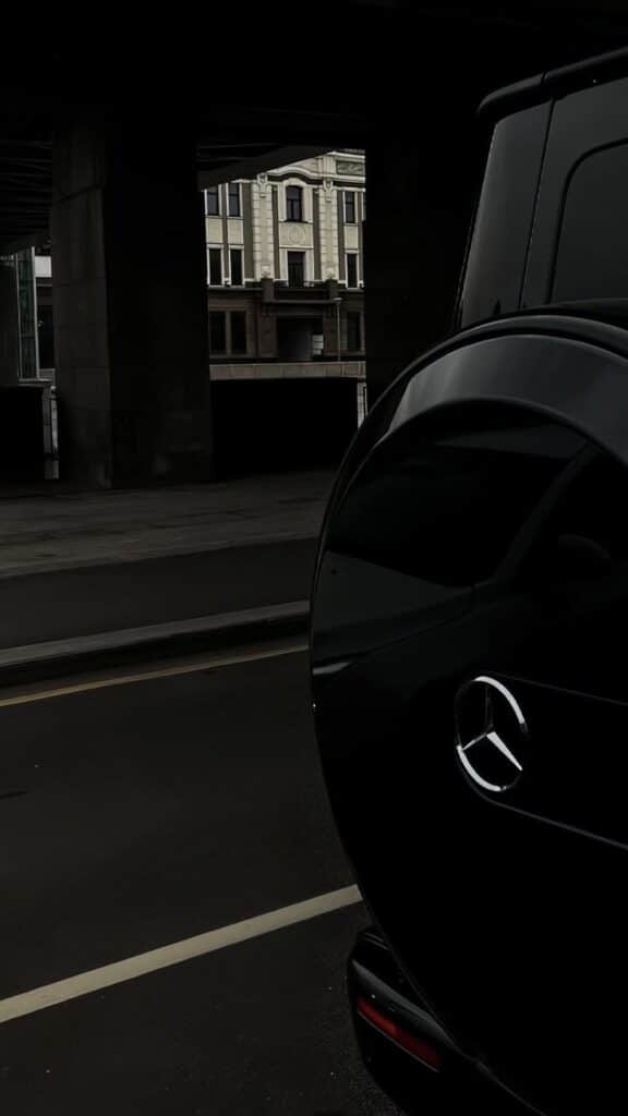Luxurious black SUV parked under a bridge, with an elegant building in the background.