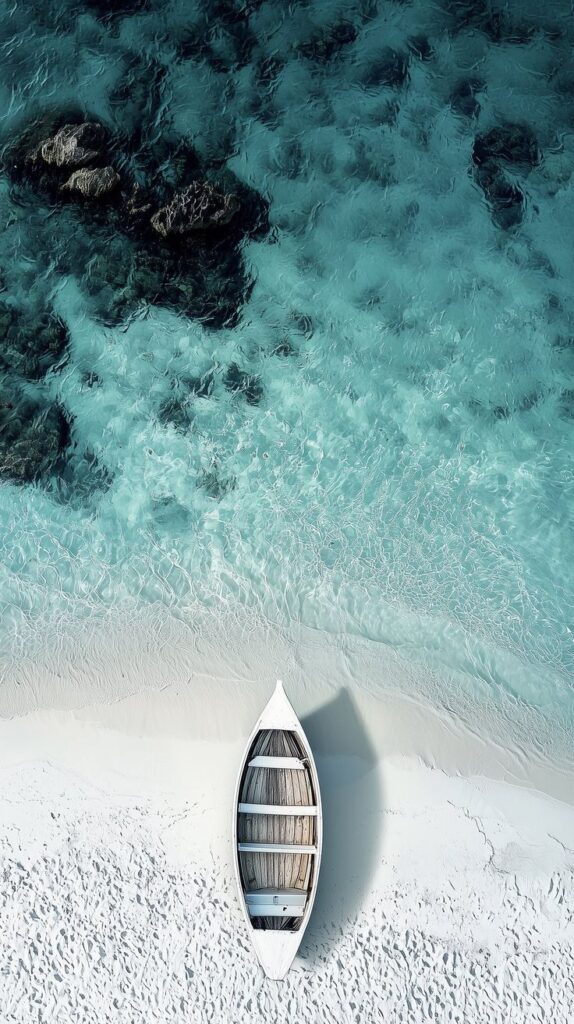 Aerial view of a white boat on a sandy beach with crystal-clear turquoise water.