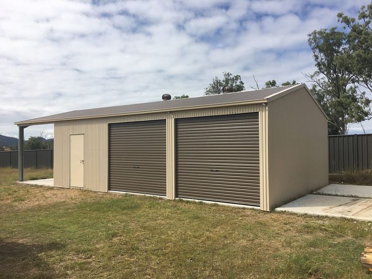 Metal garage with two roll-up doors on a grassy yard, under a partly cloudy sky.