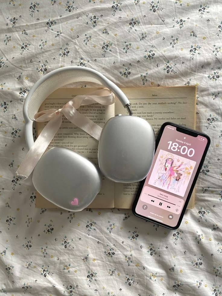 Headphones and smartphone on open book, displaying music app on floral sheet background.