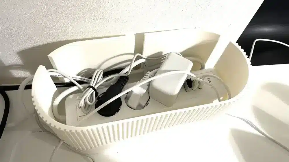Cable management box with power cords and adapters organized on a white surface.