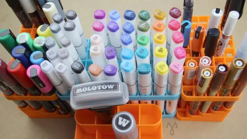 Assorted colorful markers and pens organized in orange holders on a desk, ideal for artists and designers.