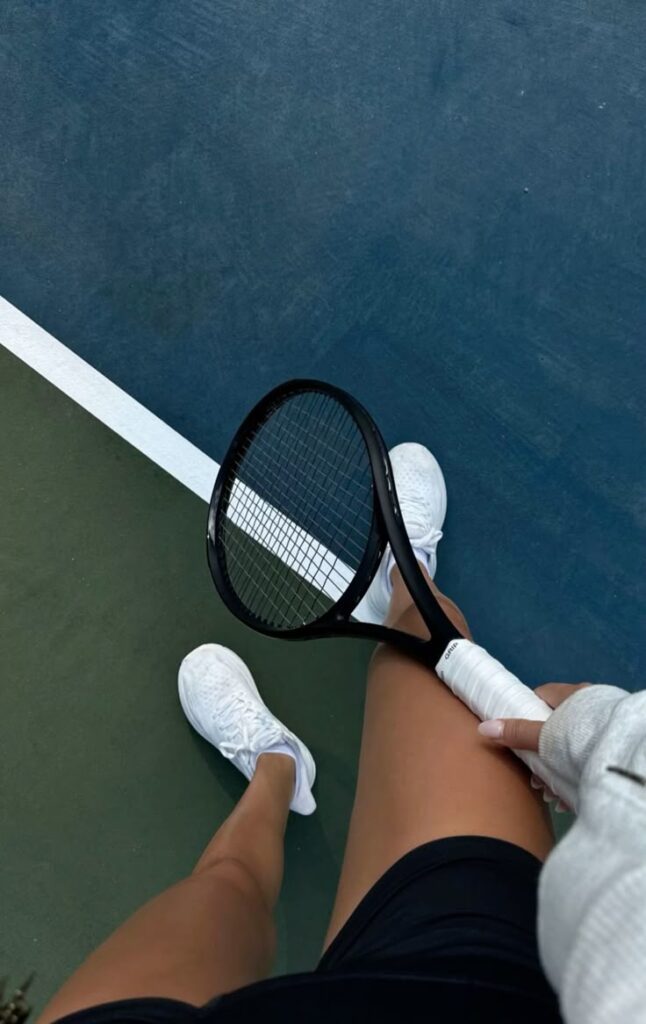 Person holding a tennis racket on a court, wearing white shoes and a sweatshirt. Ready for a match.