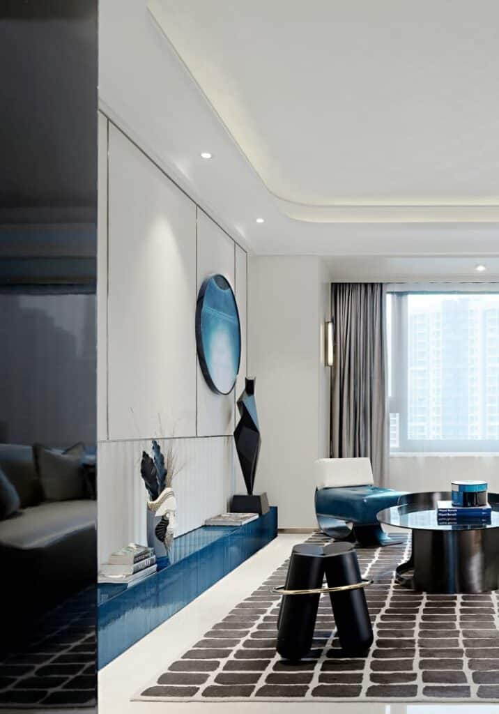 Modern living room with blue accents, abstract art, and sleek furniture under soft lighting near a large window.