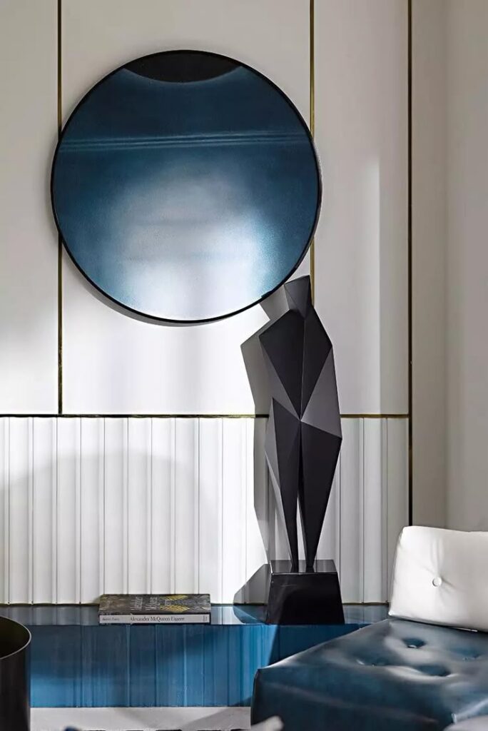 Modern interior with a blue circular mirror, abstract black sculpture, and tufted chair for stylish home decor.