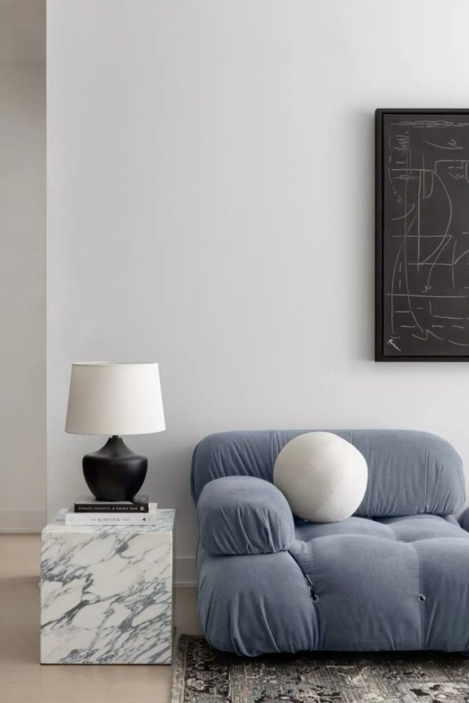 Modern living room with blue sofa, marble side table, lamp, and abstract wall art for minimalist interior design.