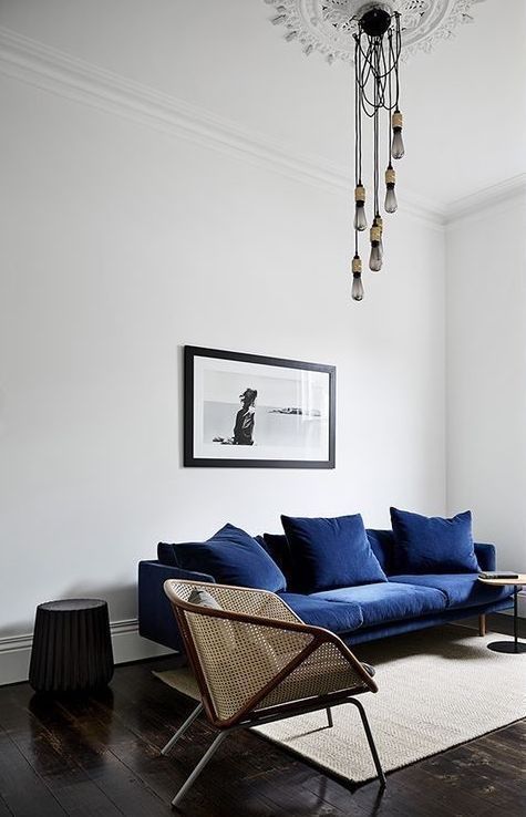 Minimalist living room with navy sofa, modern lighting, wicker chair, and wall art. Cozy and stylish interior design.
