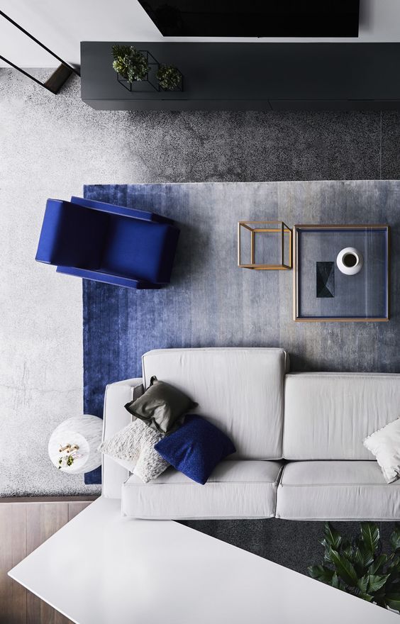 Modern living room with gray sofa, blue chair, coffee table, and decor on a gradient blue rug. Top view aesthetic.