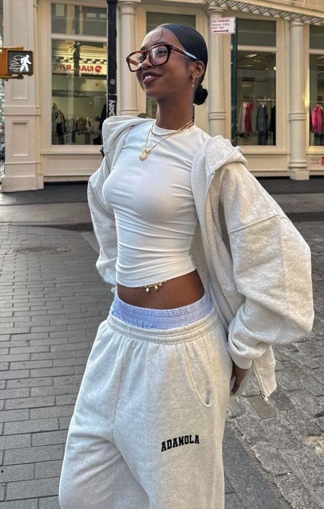 Woman in urban outfit wearing glasses, white top, and Adanola sweatpants, standing confidently on a city street.
