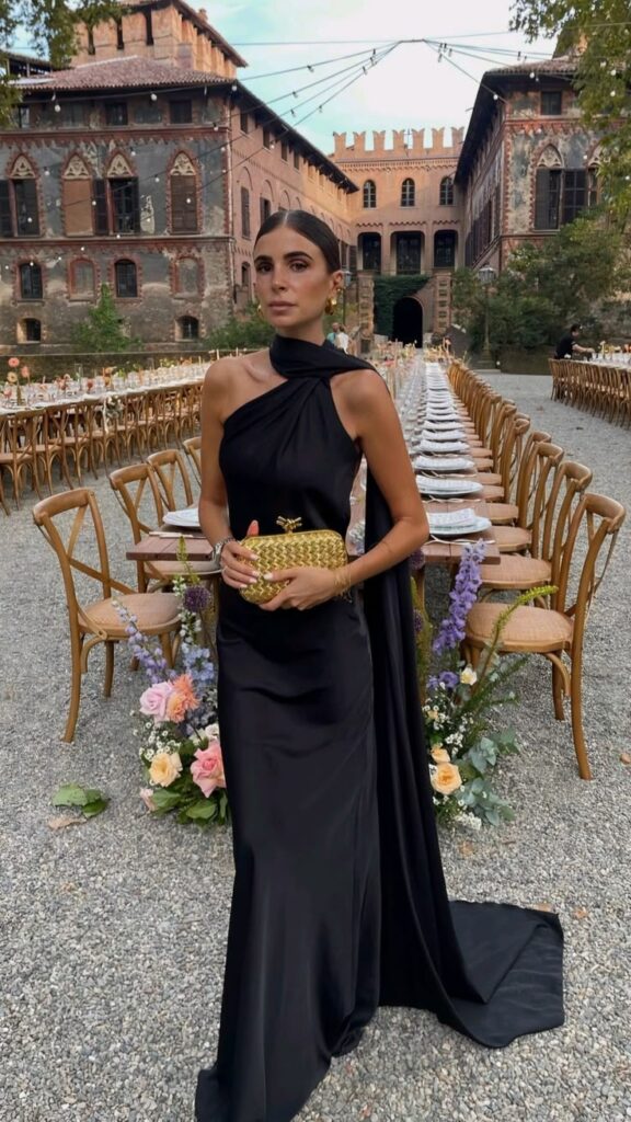 Elegant woman in a black dress at an outdoor banquet, historic building backdrop, evening wedding setting.