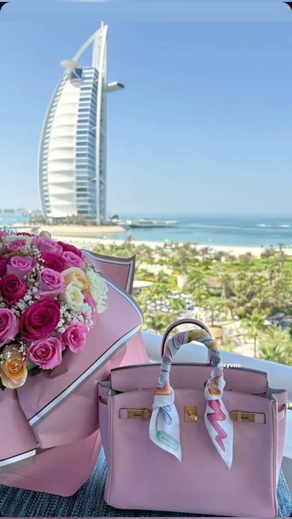 Pink handbag and rose bouquet on a balcony with Burj Al Arab in the background under a clear blue sky.